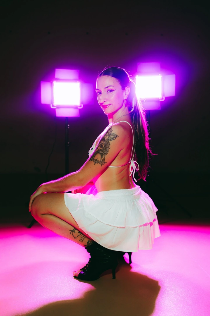 Julia Vicente en estudio, agachada con falda blanca entre dos focos magenta
